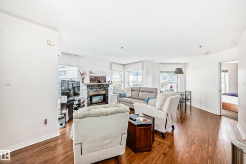 Wood-finish flooring throughout, with a fireplace featuring a stone surround and mantel - #108 12028 103 Av Nw, Edmonton, AB 