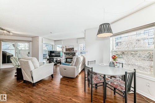 Expansive living area with wood-finish flooring, large windows, and a built-in fireplace - #108 12028 103 Av Nw, Edmonton, AB 