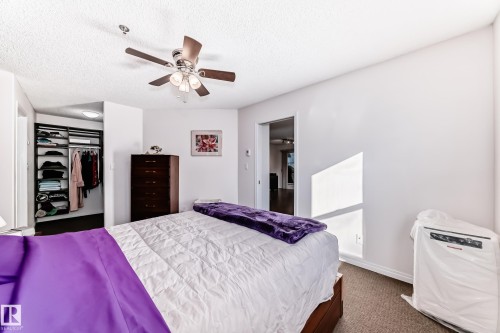 Integrated ceiling fan with light fixture, textured ceiling, built-in closet system with shelving and hanging rods, neutral wall color, and carpeted flooring - #108 12028 103 Av Nw, Edmonton, AB 