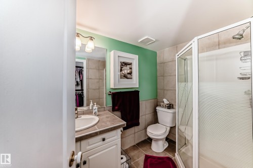 Bathroom featuring a glass-enclosed shower, white vanity with integrated sink, wall-mounted mirror, and tile flooring - #108 12028 103 Av Nw, Edmonton, AB 