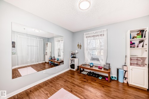 Wood-finish flooring with a full-wall mirror, built-in shelving, two windows, and a ceiling-mounted light fixture - #108 12028 103 Av Nw, Edmonton, AB 