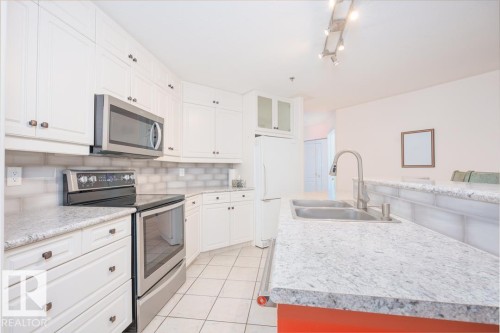 White cabinetry, stainless steel appliances, dual basin sink, tile flooring, and track lighting - #108 12028 103 Av Nw, Edmonton, AB 
