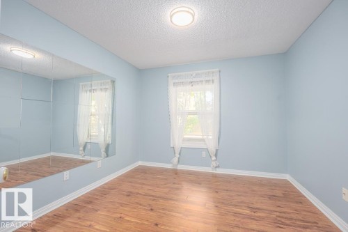 Wood-finish flooring, full-wall mirrored accent, window with natural light, and ceiling-mounted light fixture - #108 12028 103 Av Nw, Edmonton, AB 
