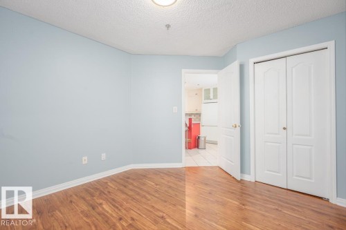 Wood-finish flooring, light blue wall paint, white baseboards, white bi-fold closet doors, and a white interior door - #108 12028 103 Av Nw, Edmonton, AB 