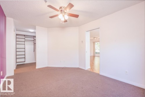 Ceiling fan with light fixture, carpeted flooring, built-in shelving and hanging rods in closet, and wood-finish flooring visible through doorway - #108 12028 103 Av Nw, Edmonton, AB 