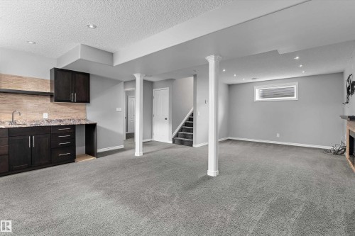 Spacious room with plush carpeting, recessed lighting, and a built-in wet bar featuring a sink, dark cabinetry, and stone-finish countertop - 20845 92A Avenue Nw, Edmonton, AB - Indoor