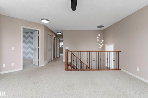 Carpeted flooring throughout, with a wood and wrought iron staircase railing, and a contemporary chandelier - 20845 92A Avenue Nw, Edmonton, AB - Indoor Photo Showing Other Room