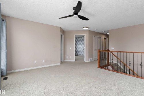 Carpeted landing area featuring a contemporary ceiling fan, flush-mount lighting, and a wood-finish railing with wrought iron balusters - 20845 92A Avenue Nw, Edmonton, AB - Indoor Photo Showing Other Room