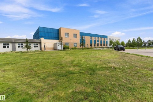 Exterior building featuring a combination of brick, metal siding, and stucco finishes, multiple window installations, and a surrounding green space - 20845 92A Avenue Nw, Edmonton, AB - Outdoor