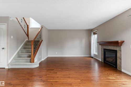Hardwood flooring, natural stone fireplace with a wood mantle, carpeted staircase with wood and wrought iron railing, and neutral wall paint - 20845 92A Avenue Nw, Edmonton, AB - Indoor With Fireplace