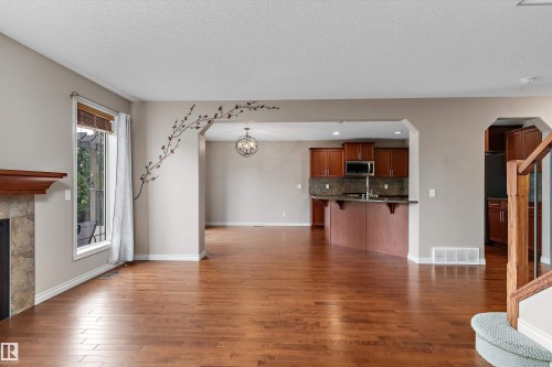Wood-finish flooring throughout, fireplace with a stone surround and wood mantel, arched entryways, kitchen with wood cabinetry and stainless steel appliances, and a built-in kitchen island - 20845 92A Avenue Nw, Edmonton, AB - Indoor With Fireplace