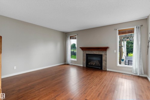 Hardwood-style flooring, stone-clad fireplace with wood mantel, and multiple windows - 20845 92A Avenue Nw, Edmonton, AB - Indoor Photo Showing Living Room With Fireplace
