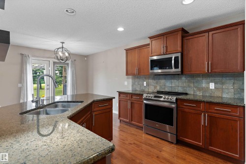 Kitchen featuring wood cabinetry, stainless steel appliances, stone countertops, and a tile backsplash - 20845 92A Avenue Nw, Edmonton, AB - Indoor Photo Showing Kitchen With Double Sink