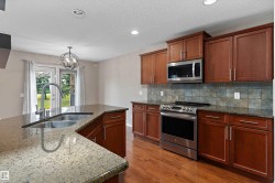 Kitchen featuring wood cabinetry, stainless steel appliances, stone countertops, and a tile backsplash - 
