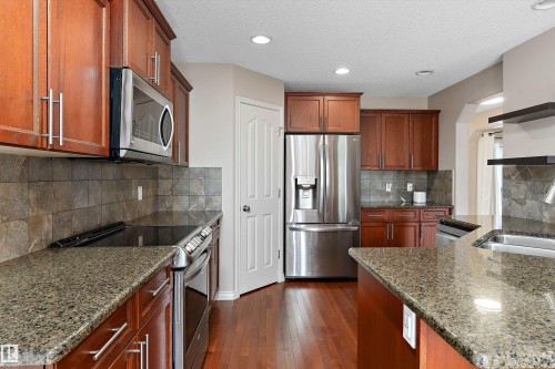 Kitchen featuring wood-finish cabinetry, stainless steel appliances, granite countertops, tile backsplash, and wood-finish flooring - 20845 92A Avenue Nw, Edmonton, AB - Indoor Photo Showing Kitchen With Upgraded Kitchen