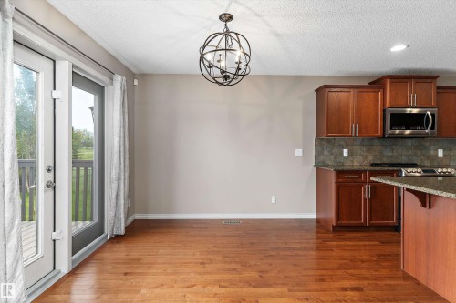 Warm wood-finish flooring, a contemporary orb chandelier, and rich wood cabinetry with stainless steel appliances - 20845 92A Avenue Nw, Edmonton, AB - Indoor Photo Showing Kitchen