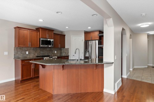 Kitchen featuring wood-finish cabinetry, stainless steel appliances, central island with sink, stone-finish countertops, and wood-finish flooring - 20845 92A Avenue Nw, Edmonton, AB - Indoor Photo Showing Kitchen