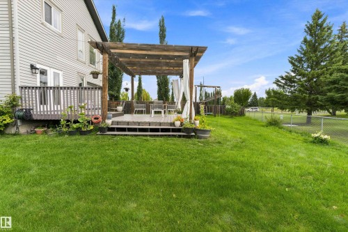Expansive lawn area with a two-tiered wooden deck, featuring a pergola with draped fabric accents, and a chain-link fence - 20845 92A Avenue Nw, Edmonton, AB - Outdoor With Deck Patio Veranda