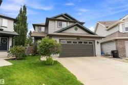 Two-story residence featuring light gray siding, dark green trim, an attached garage with a dark panel door, and a concrete driveway - 