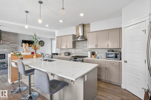 Open-concept kitchen with a large central island, light-toned cabinetry, stainless steel appliances, and wood-finish flooring - 923 174St Sw, Edmonton, AB 