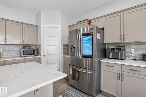 Kitchen featuring an island with a light-toned countertop, upper and lower cabinetry, a tile backsplash, and wood-finish flooring - 923 174St Sw, Edmonton, AB 