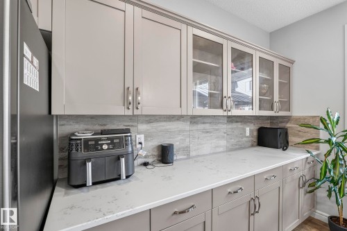 White countertop, light gray cabinetry, glass-front upper cabinets, light gray tile backsplash, and stainless steel hardware - 923 174St Sw, Edmonton, AB 
