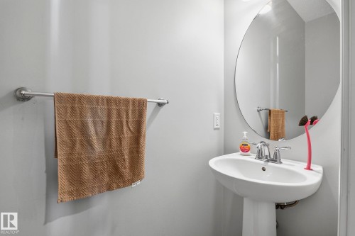 White pedestal sink with chrome faucet, complemented by a large oval wall mirror - 923 174St Sw, Edmonton, AB 