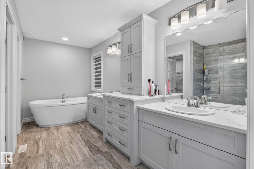 Freestanding soaking tub, dual vanities with undermount sinks, wood-finish tile flooring, walk-in shower with tiled walls, and built-in storage cabinetry - 923 174St Sw, Edmonton, AB 