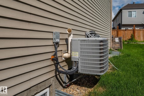 Horizontal siding exterior with a ground-mounted HVAC unit and a basement window well - 923 174St Sw, Edmonton, AB 