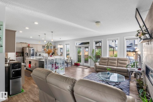 Open-concept living space with wood-finish flooring, a contemporary kitchen island with pendant lighting, and multiple large windows - 923 174St Sw, Edmonton, AB 