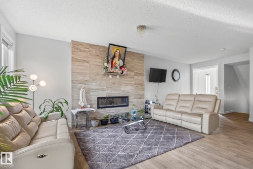 Light-toned wood-finish flooring, recessed electric fireplace with a stacked stone surround, white trim, and a ceiling-mounted light fixture - 923 174St Sw, Edmonton, AB 
