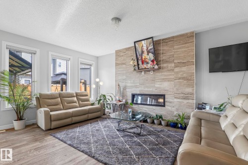 Recessed linear fireplace with a stone tile surround, wood-finish flooring, multiple large windows, and a ceiling-mounted light fixture - 923 174St Sw, Edmonton, AB 