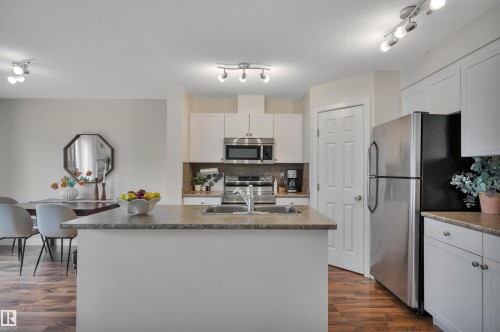 Kitchen featuring an island with an undermount sink, stainless steel appliances, white cabinetry, and wood-finish flooring - 17321 8A Avenue Sw, Edmonton, AB - Indoor Photo Showing Kitchen With Stainless Steel Kitchen With Double Sink