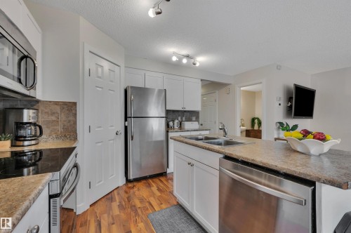 White cabinetry, stainless steel appliances, dual basin sink, wood-finish flooring, and track lighting - 17321 8A Avenue Sw, Edmonton, AB - Indoor Photo Showing Kitchen With Stainless Steel Kitchen With Double Sink