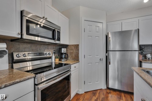 Kitchen featuring stainless steel appliances, white cabinetry, dark stone-look backsplash, and wood-finish flooring - 17321 8A Avenue Sw, Edmonton, AB - Indoor Photo Showing Kitchen With Stainless Steel Kitchen
