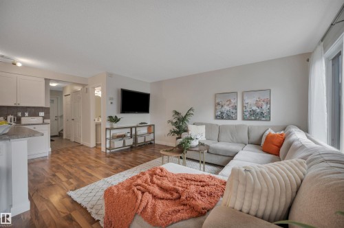 Open-concept living area featuring wood-finish flooring, white cabinetry, a built-in kitchen island, and large windows - 17321 8A Avenue Sw, Edmonton, AB - Indoor Photo Showing Living Room