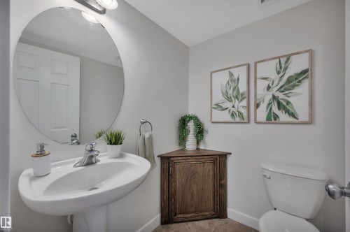 Pedestal sink with chrome faucet, oval wall mirror, and a corner wood-finish cabinet - 17321 8A Avenue Sw, Edmonton, AB - Indoor Photo Showing Bathroom