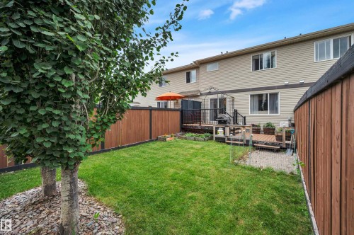 Private backyard featuring a wooden deck, slatted wood fence, and mature trees with rock ground cover - 17321 8A Avenue Sw, Edmonton, AB - Outdoor With Deck Patio Veranda
