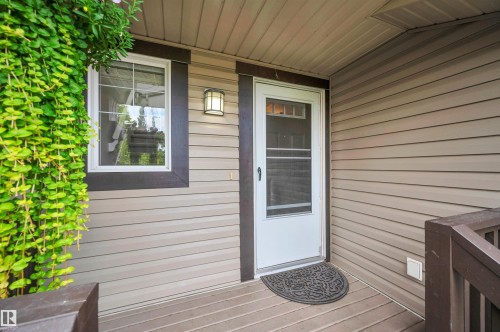 Vinyl siding exterior with a white entry door, an exterior wall sconce, and a covered porch with wood-finish decking - 17321 8A Avenue Sw, Edmonton, AB - Outdoor With Exterior