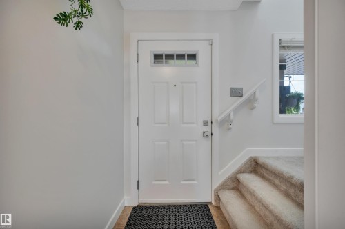 Entry door with decorative lites, framed window, and carpeted stairs with a white handrail - 17321 8A Avenue Sw, Edmonton, AB - Indoor Photo Showing Other Room