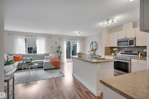 Spacious open-concept living area with wood-finish flooring, white cabinetry, stainless steel appliances, and a kitchen island with integrated sink - 17321 8A Avenue Sw, Edmonton, AB - Indoor Photo Showing Other Room