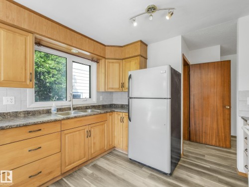 Wood-finish cabinetry, tile backsplash, laminate countertop, double-basin stainless steel sink, wood-finish flooring - 16428 88 Avenue Nw, Edmonton, AB - Indoor Photo Showing Kitchen With Double Sink