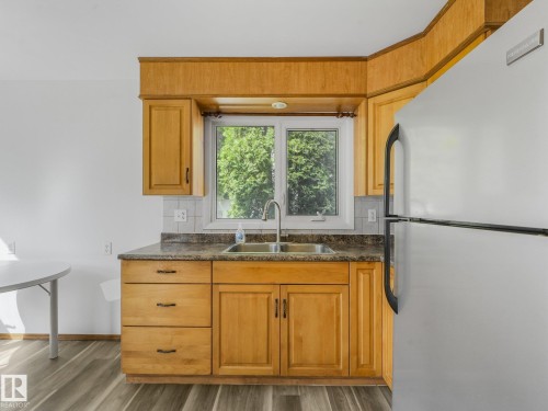 Wood-finish flooring, light wood cabinetry, white tile backsplash, stainless steel sink, and a stainless steel refrigerator - 16428 88 Avenue Nw, Edmonton, AB - Indoor Photo Showing Kitchen With Double Sink