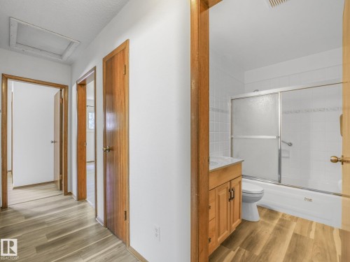 Wood-finish flooring throughout, solid wood doors, and a bathroom featuring a wood-finish vanity with a white countertop and a tub with a sliding glass enclosure - 16428 88 Avenue Nw, Edmonton, AB - Indoor