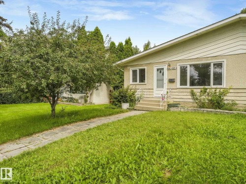 Single-story residence featuring light-colored siding and stucco, multiple windows, a front entry with handrails, and a mature tree in the foreground - 16428 88 Avenue Nw, Edmonton, AB - Outdoor
