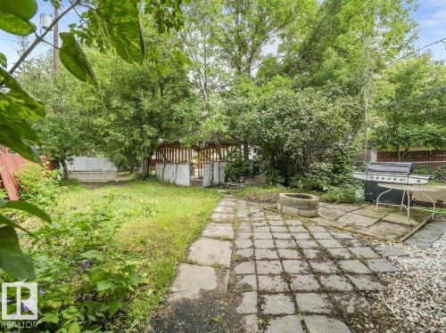 Expansive backyard featuring a stone paver patio, a concrete block fire pit, and a wooden gazebo structure - 16428 88 Avenue Nw, Edmonton, AB - Outdoor