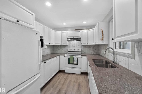 White cabinetry with dark hardware, stone-look countertops, stainless steel double basin sink, light wood-finish flooring, and recessed lighting - #28 3645 145 Av Nw, Edmonton, AB - Indoor Photo Showing Kitchen With Double Sink