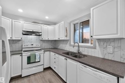 White cabinetry with dark hardware, stone-finish countertops, stainless steel double basin sink, white electric range, and wood-finish flooring - 