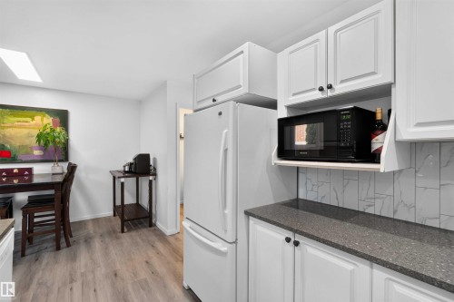 Kitchen featuring white cabinetry, gray speckled countertops, a subway tile backsplash, and wood-finish flooring - #28 3645 145 Av Nw, Edmonton, AB - Indoor Photo Showing Kitchen