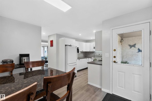 Open-concept living area featuring wood-finish flooring, white cabinetry, dark countertops, and a white refrigerator - #28 3645 145 Av Nw, Edmonton, AB - Indoor Photo Showing Kitchen